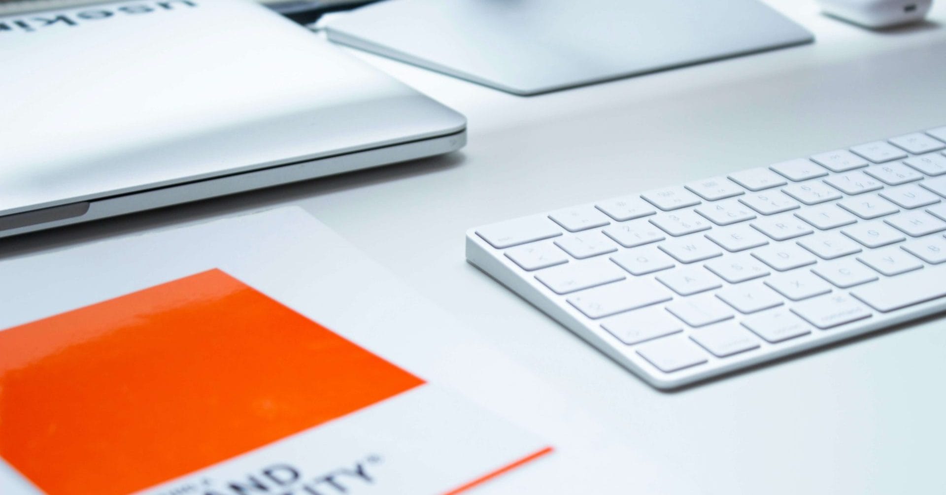 White desk with a keyboard, laptop, monitor, and a book titled "Brand Identity.